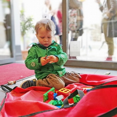 Ein Junge in einer grünen Jacke sitzt auf dem Boden und spielt mit buntem Spielzeug