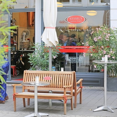 Die Ladenterasse vor Kessel´s Espresso Studio mit mehreren Pflanzen, Tischen und Bänken